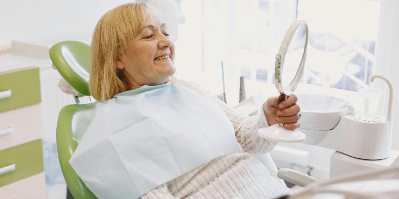 Older woman smiling while checking her new dentures in dental clinic mirror