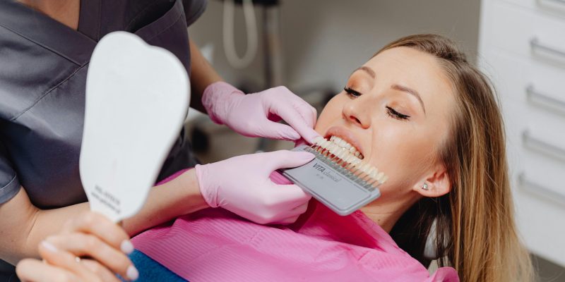 Patient comparing tooth shades with dentist using dental mirror